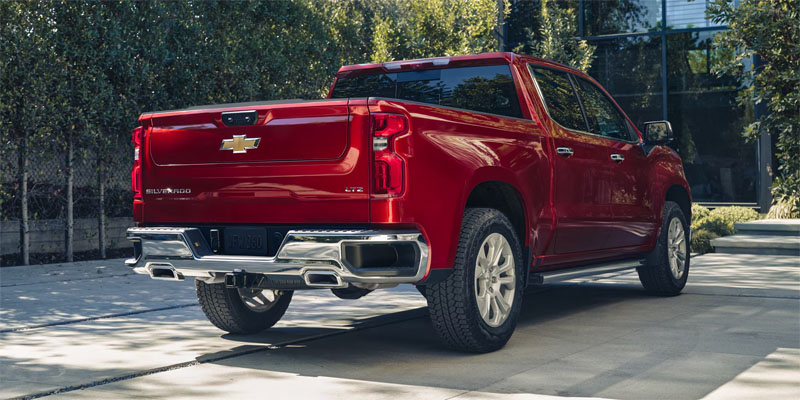 A red Chevrolet Silverado pickup truck parked outside a modern building with a clear view of the rear.