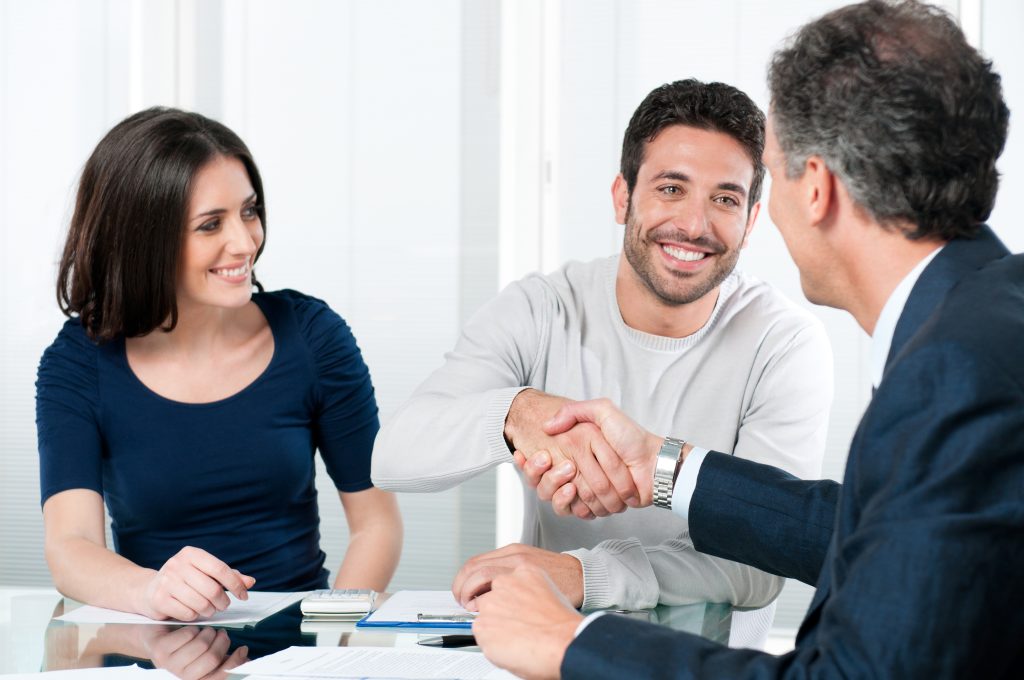 A couple shaking hands with a salesperson at a desk, finalizing a deal.